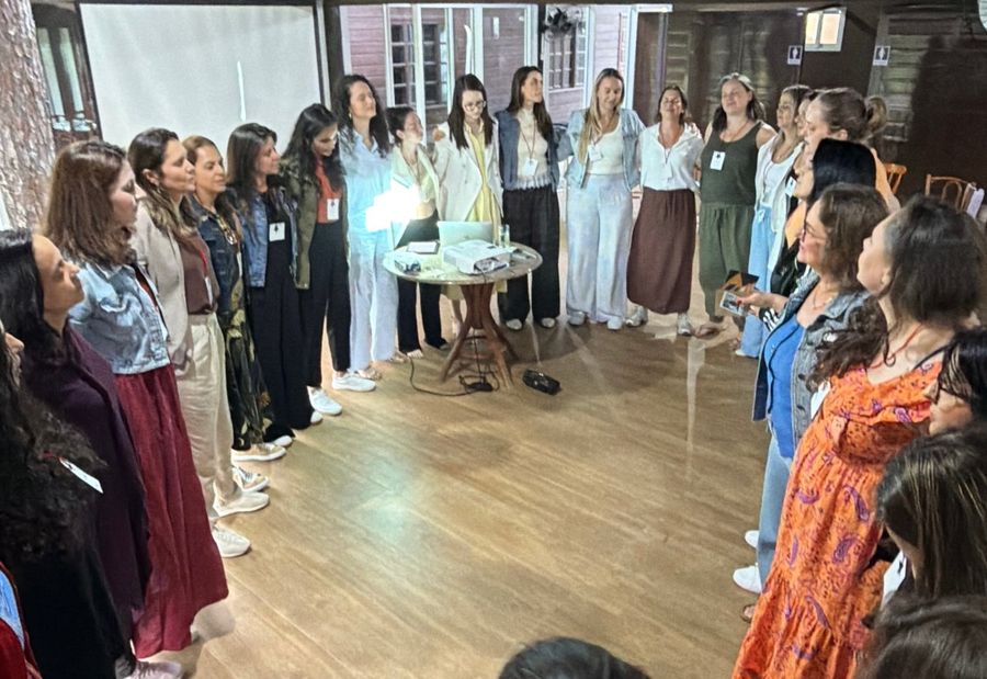 Alunas em roda num encontro presencial, numa sala com piso de madeira